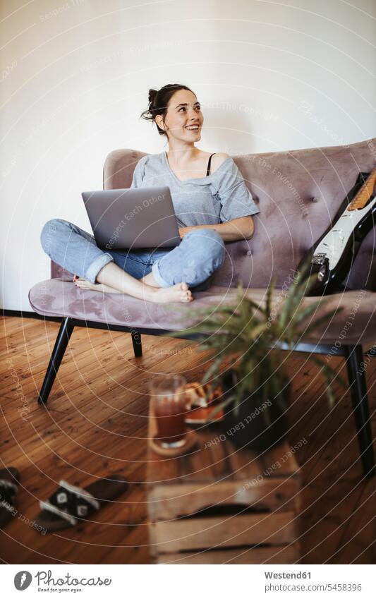 Porträt einer lächelnden jungen Frau, die zu Hause auf einer Couch mit Laptop sitzt Leute Menschen People Person Personen erwachsen Erwachsene Frauen weiblich