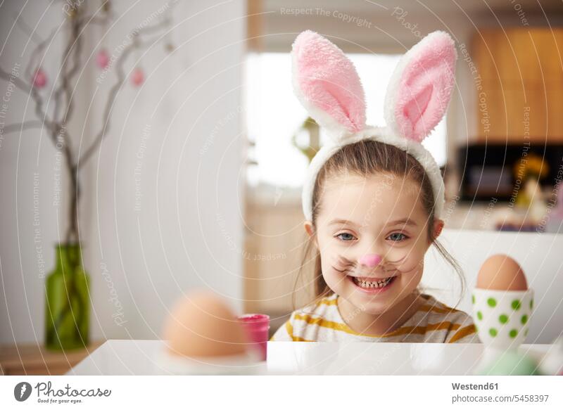Porträt eines lächelnden Mädchens mit Hasenohren, das mit Ostereiern am Tisch sitzt weiblich Häschenohren Portrait Porträts Portraits Ostern Osterfest Kind