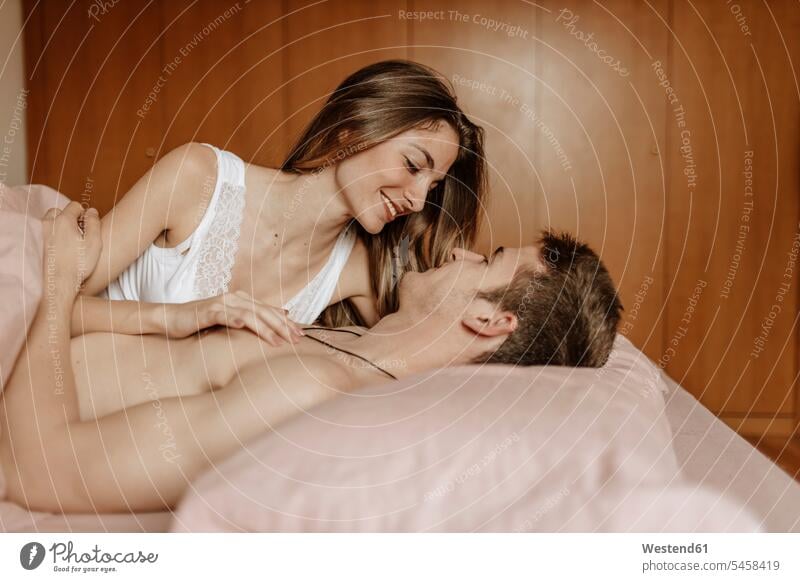 Glückliches junges Paar liegt im Bett Betten anfassen Berührung knuddeln schmusen freuen Frohsinn Fröhlichkeit Heiterkeit geniessen Genuss glücklich sein