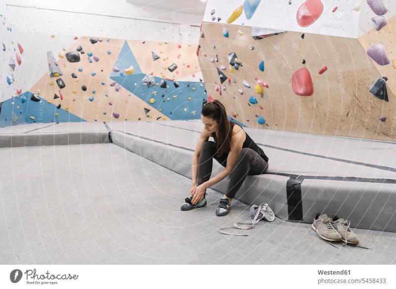 Frau bereitet sich auf das Klettern an der Wand vor und zieht Schuhe an (value=0) steigen sitzend sitzt Muße trainieren Waende Wände drinnen Innenaufnahmen