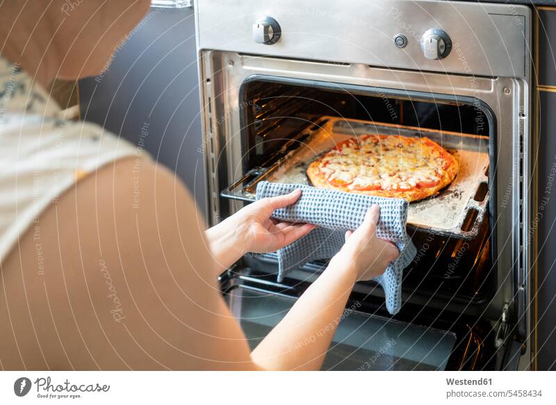 Schnittansicht einer Frau, die ein Tablett mit gebackener Pizza aus dem Ofen nimmt daheim zu Hause heiss Hitze Muße Lifestyles Aktivitaet Aktivität Handeln