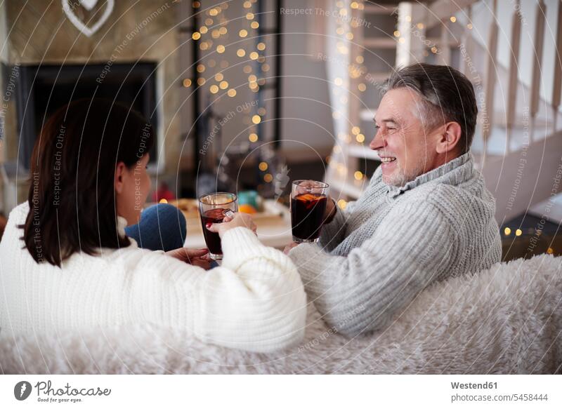 Glückliches reifes Paar mit heißen Getränken im Wohnzimmer entspannt entspanntheit relaxt Heißgetränk heißes Getränk Pärchen Paare Partnerschaft sitzen sitzend