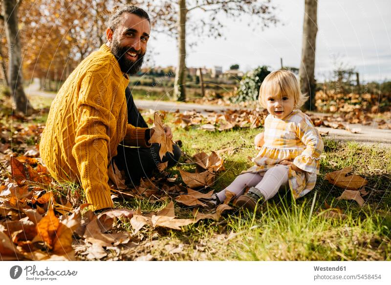 Vater und Tochter sitzen auf Wiese mit Herbstlaub, Morgen Tag im Park morgens früh Frühe Blatt Blaetter Blätter Wiesen Papas Väter Vati Vatis Papis Töchter