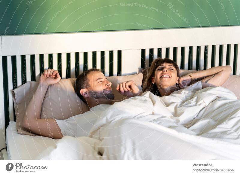 Lächelndes Paar, das langsam aufwacht, während es auf dem Bett zu Hause liegt Farbaufnahme Farbe Farbfoto Farbphoto Innenaufnahme Innenaufnahmen innen drinnen