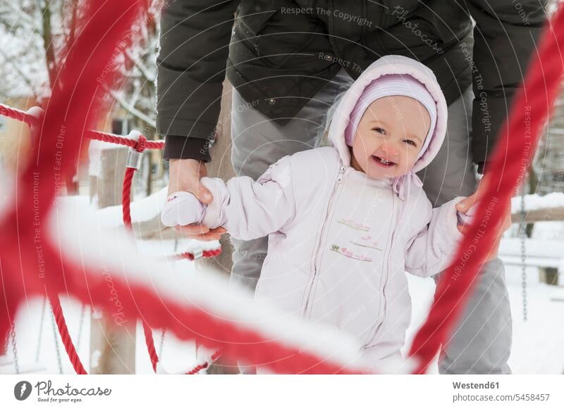 Porträt eines lächelnden Mädchens mit Vater auf dem Spielplatz im Winter Papas Väter Vati Vatis Papis Portrait Porträts Portraits winterlich Winterzeit Baby