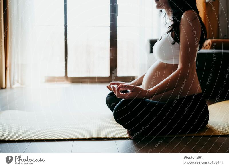 Schwangere Frau meditiert, während sie zu Hause auf einer Fitnessmatte sitzt Farbaufnahme Farbe Farbfoto Farbphoto Innenaufnahme Innenaufnahmen innen drinnen