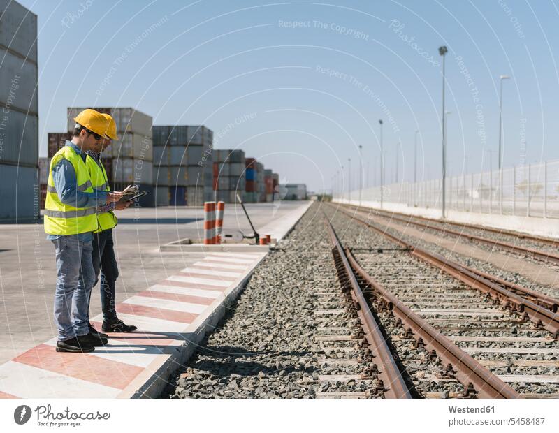 Arbeiter vor Frachtcontainern in der Nähe von Bahngleisen auf einem Industriegelände Spanien Arbeitsschutz besprechen diskutieren Besprechung Containerterminal