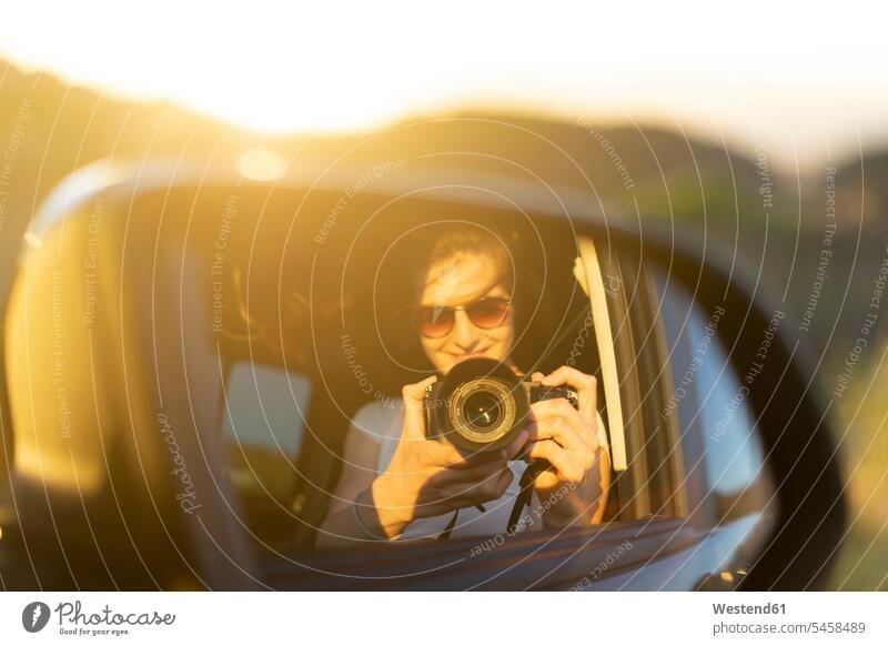 Junge Frau beim Fotografieren ihres Spiegelbildes in ihrem Auto weiblich Frauen Sommer Sommerzeit sommerlich Wagen PKWs Automobil Autos Urlaub Ferien