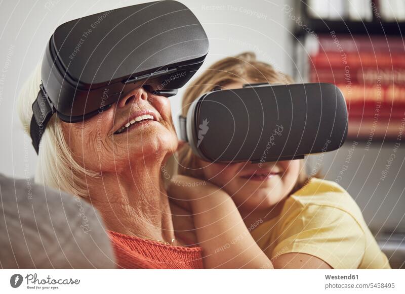 Großmutter benutzt VR-Brille mit ihrem Enkel daheim zu Hause drinnen Innenaufnahmen Generation Leute Menschen People Person Personen Familien Grosseltern