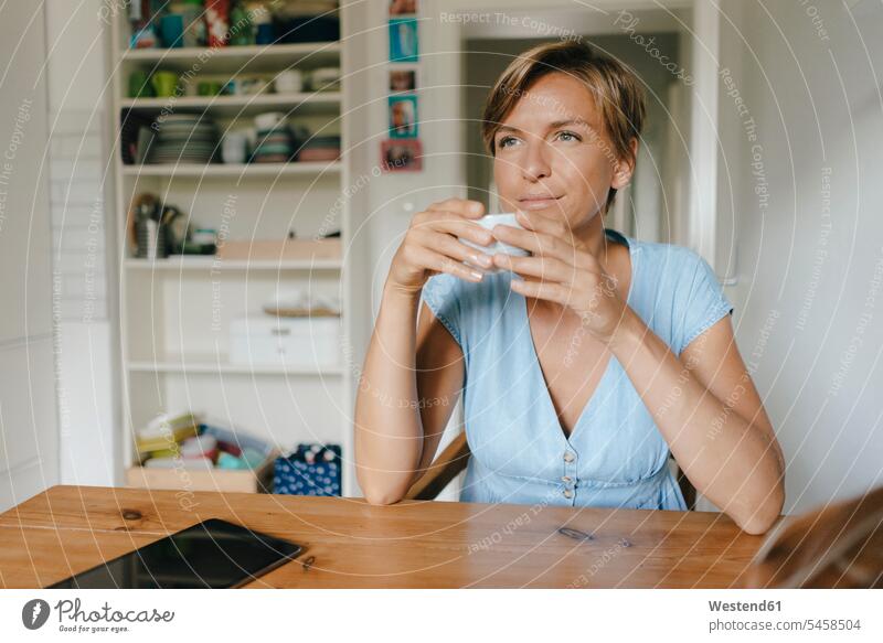 Frau sitzt am Tisch zu Hause mit einer Tasse Kaffee Kaffeetasse Kaffeetassen Zuhause daheim weiblich Frauen sitzen sitzend Tische Tassen Getränk Getraenk