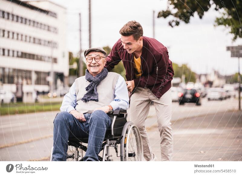 Junger Mann schiebt glücklichen älteren Mann im Rollstuhl Leute Menschen People Person Personen Europäisch Kaukasier kaukasisch 2 2 Menschen 2 Personen zwei