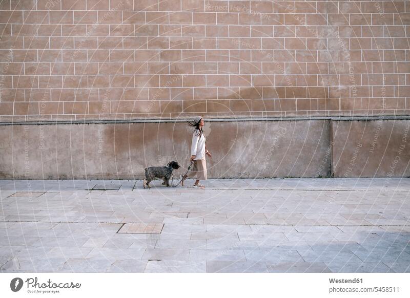 Junge Frau geht mit ihrem Hund in der Stadt spazieren Tiere Tierwelt Haustiere Hunde Jacken Mützen Muße außen draußen im Freien staedtisch städtisch Urbanitaet