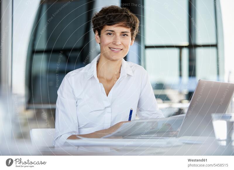 Porträt der zuversichtlich Geschäftsfrau sitzt am Schreibtisch im Büro mit Laptop und Dokument Arbeitstisch Schreibtische Office Büros sitzen sitzend Notebook