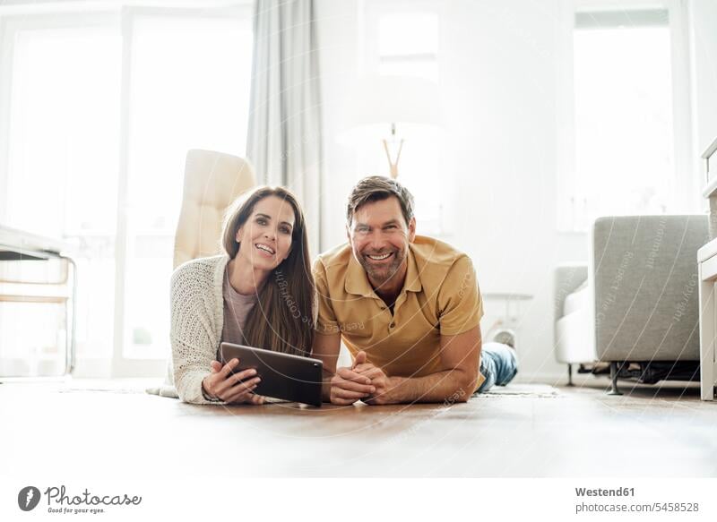 Lächelnde reifen Mann und Frau mit digitalen Tablette auf dem Boden liegend in der Wohnung Farbaufnahme Farbe Farbfoto Farbphoto Tag Tageslichtaufnahme