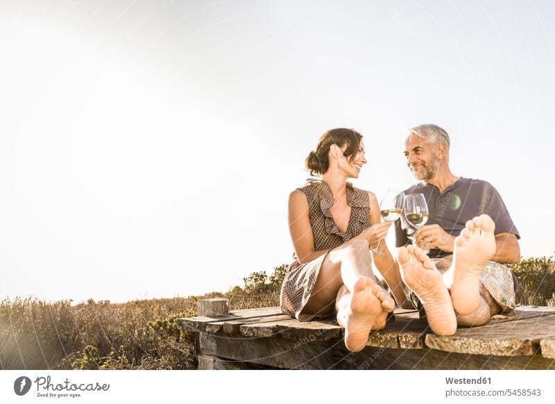 Glückliches Paar sitzt auf der Strandpromenade an der Küste und genießt ein Glas Weißwein Touristen sitzend abends Jahreszeiten sommerlich Sommerzeit entspannen