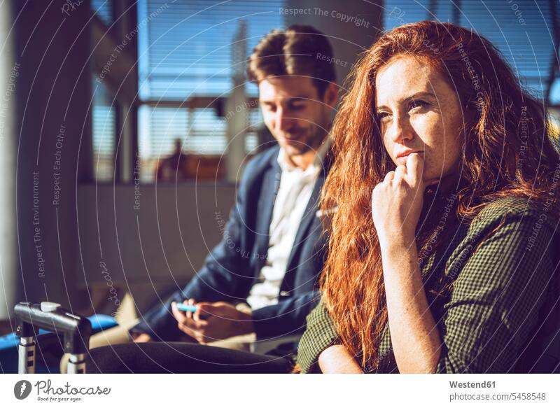 Nachdenkliche Geschäftsfrau sitzt mit Mann im Abflugbereich des Flughafens Farbaufnahme Farbe Farbfoto Farbphoto Innenaufnahme Innenaufnahmen innen drinnen Tag