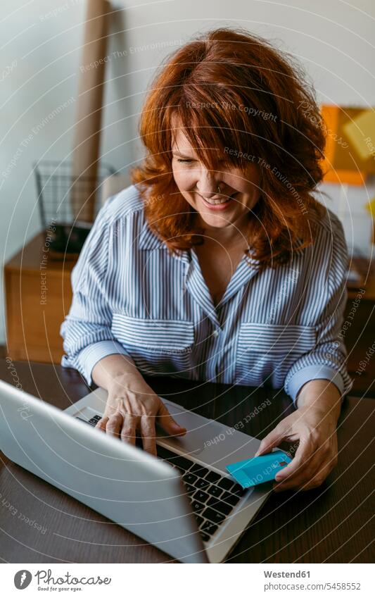 Lächelnde Frau beim Online-Shopping am Laptop, während sie zu Hause sitzt Farbaufnahme Farbe Farbfoto Farbphoto Innenaufnahme Innenaufnahmen innen drinnen Tag