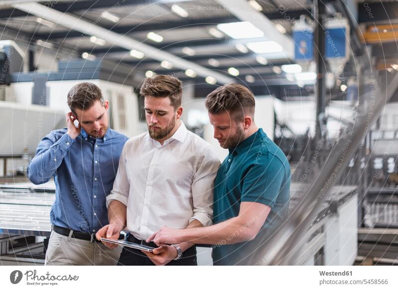 Drei Männer teilen sich Tabletten in der Fabrikhalle Kollegen Arbeitskollegen Produktionshalle Montagehalle Mann männlich Teilen Sharing Fabriken