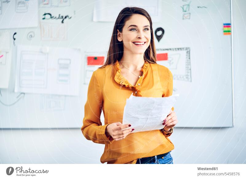 Lächelnde Geschäftsfrau mit Papieren stehend am Whiteboard, die eine Präsentation leitet Büro Office Büros steht lächeln Praesentationen Präsentationen leiten