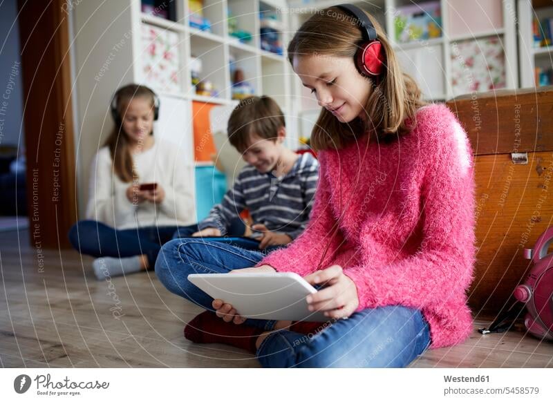 Geschwister spielen zu Hause mit ihren digitalen Tablets, sitzen auf dem Boden Fokus Auf Den Vordergrund Freizeitkleidung Ganzkörperansicht braune Haare