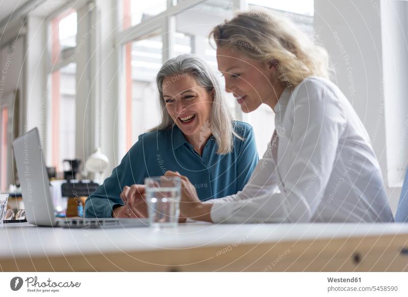 Zwei glückliche Geschäftsfrauen benutzen gemeinsam einen Laptop am Schreibtisch im Büro Generation Job Berufe Berufstätigkeit Beschäftigung Jobs geschäftlich
