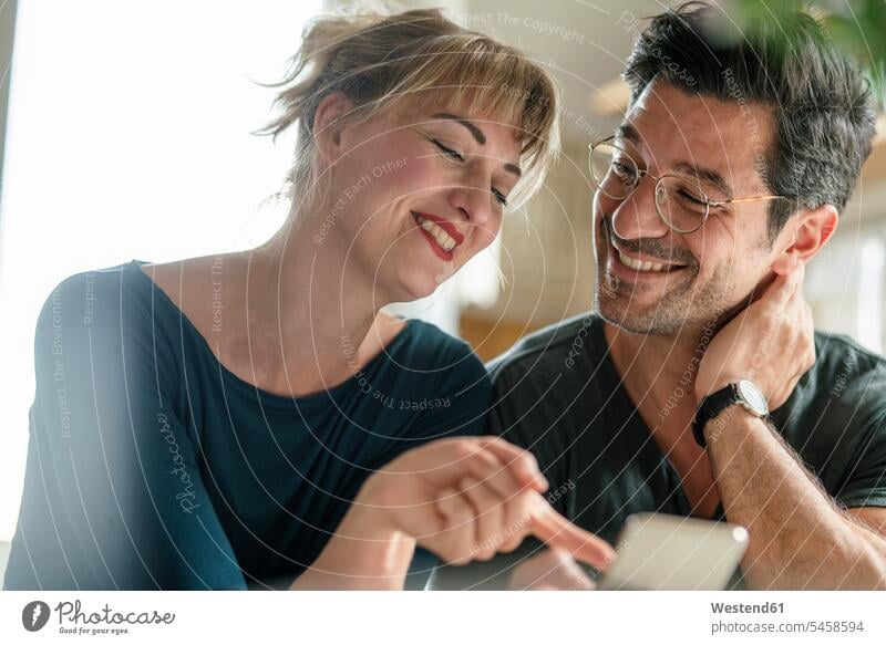 Glückliches Paar nutzt Smartphone zu Hause Informationen Telekommunikation telefonieren Handies Handys Mobiltelefon Mobiltelefone Brillen reden freuen Frohsinn
