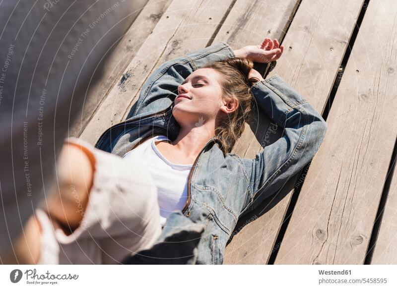 Entspannte junge Frau auf Holzbrettern im Sonnenschein liegend weiblich Frauen entspannt entspanntheit relaxt Sonnenlicht Holzplatten liegt Erwachsener