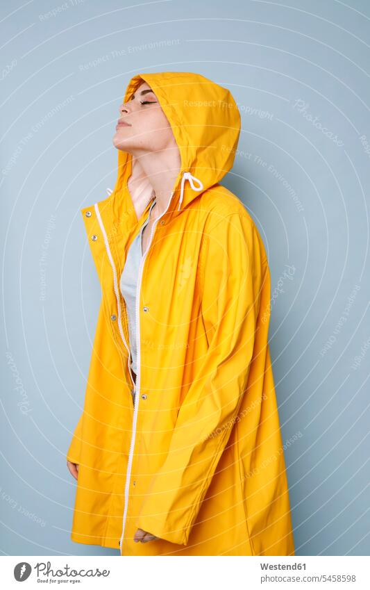 Junge Frau trägt gelben Regenmantel vor blauem Hintergrund Regenjacke Regenjacken weiblich Frauen gelber gelbes Erwachsener erwachsen Mensch Menschen Leute