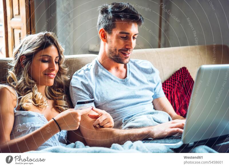 Junges Paar sitzt auf der Couch zu Hause mit Kreditkarte und Laptop Bankwesen EC-Karte Kreditkarten Karten Couches Liege Sofas Rechner Laptops Notebook