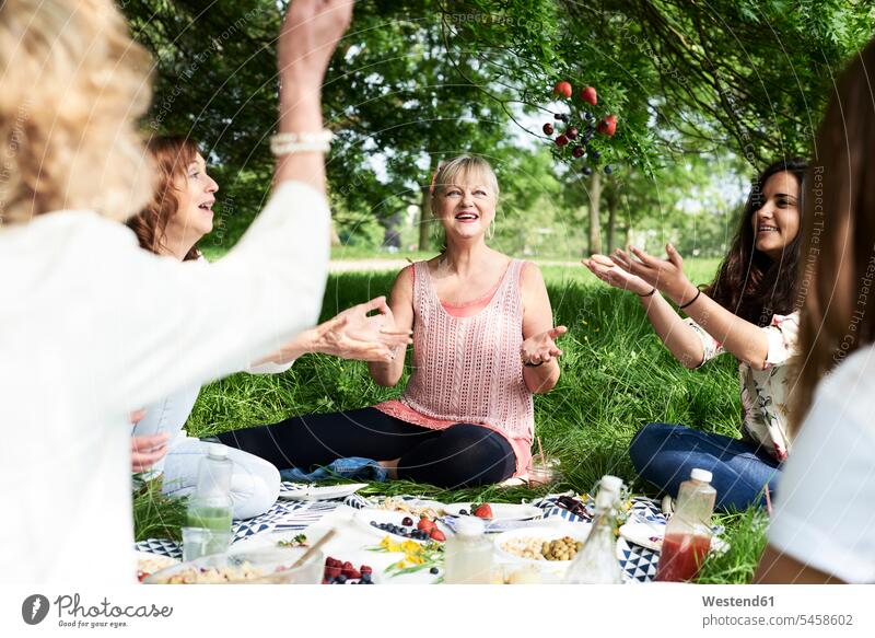 Glückliche Frauen werfen Beeren in die Luft bei einem Picknick im Park glücklich glücklich sein glücklichsein Freundinnen picknicken Parkanlagen Parks weiblich