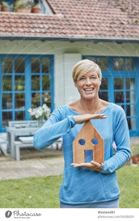Porträt einer lächelnden Frau, die vor ihrem Haus haltenden Hausmodell steht Portrait Porträts Portraits Modell Modelle stehen stehend weiblich Frauen Häuser