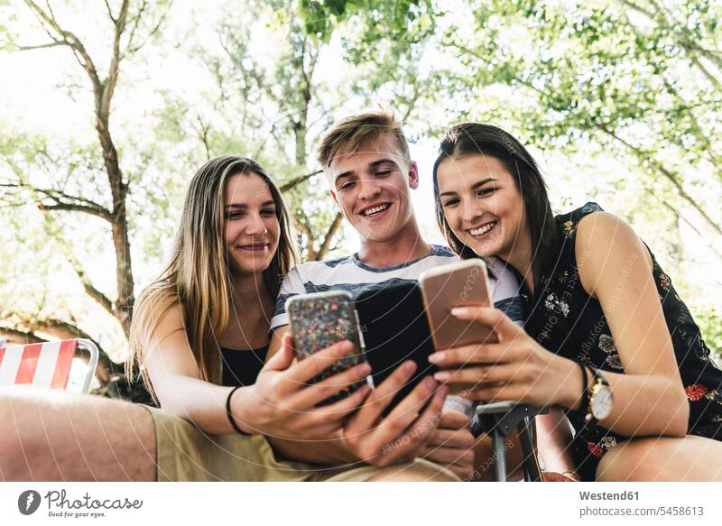 Drei glückliche Freunde schauen draußen auf Mobiltelefone Glück glücklich sein glücklichsein Handy Handies Handys ansehen Gruppe Gruppe von Menschen