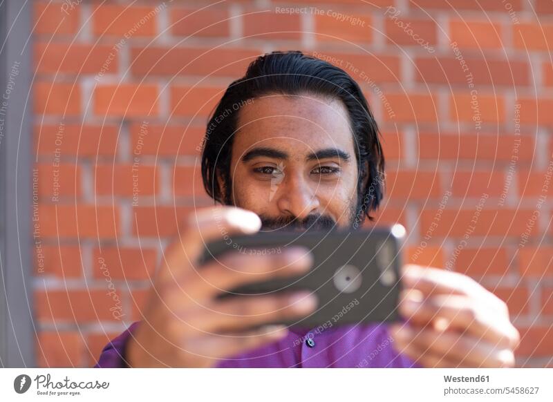 Junger Mann macht ein Selfie mit seinem Smartphone Job Berufe Berufstätigkeit Beschäftigung Jobs Techniken Technologie Techniker Bilder Bildnis Fotos