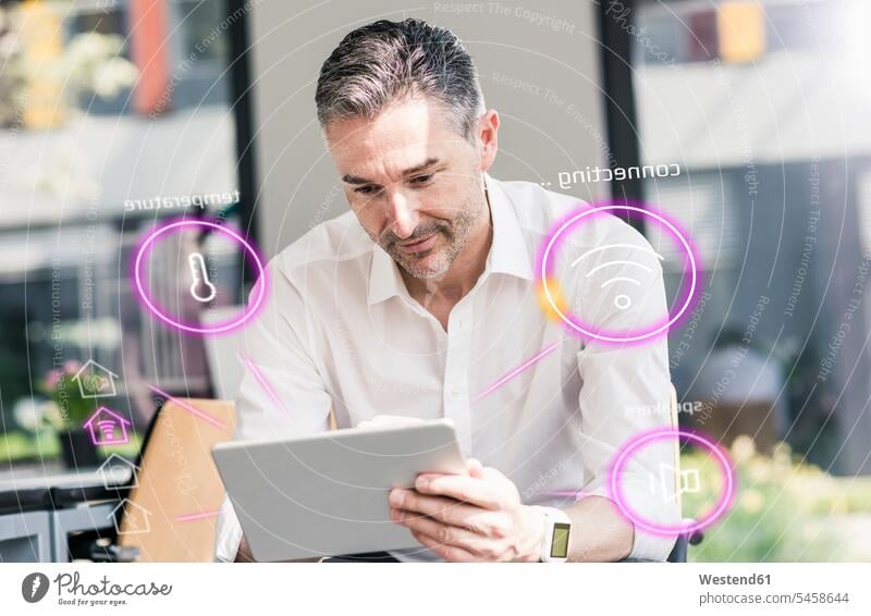 Mann sitzt im Büro und benutzt ein digitales Tablet zur Fernsteuerung seines intelligenten Hauses Office Büros einschalten anschalten Smart Home smarthome