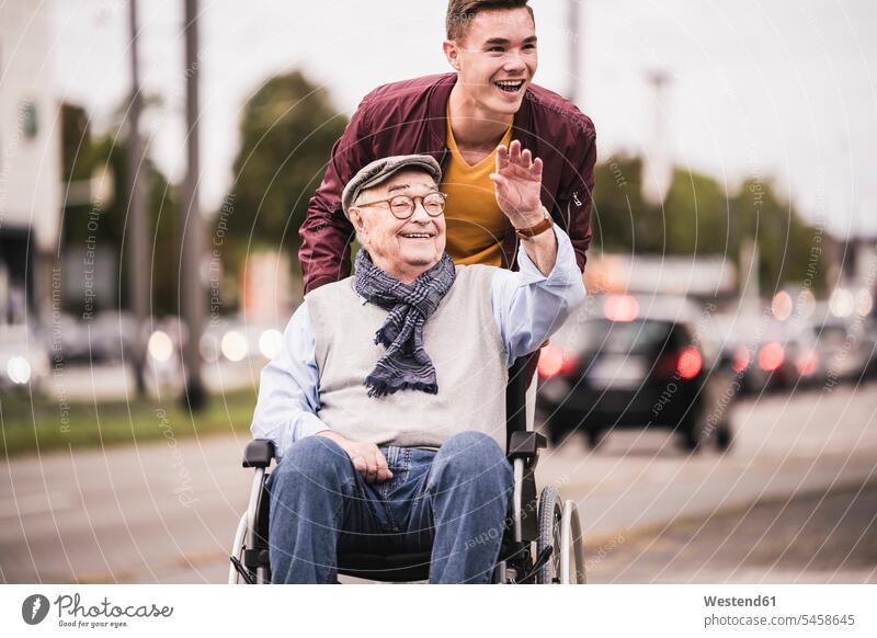 Porträt eines lachenden jungen Mannes, der einen glücklichen älteren Mann im Rollstuhl schiebt Leute Menschen People Person Personen Europäisch Kaukasier