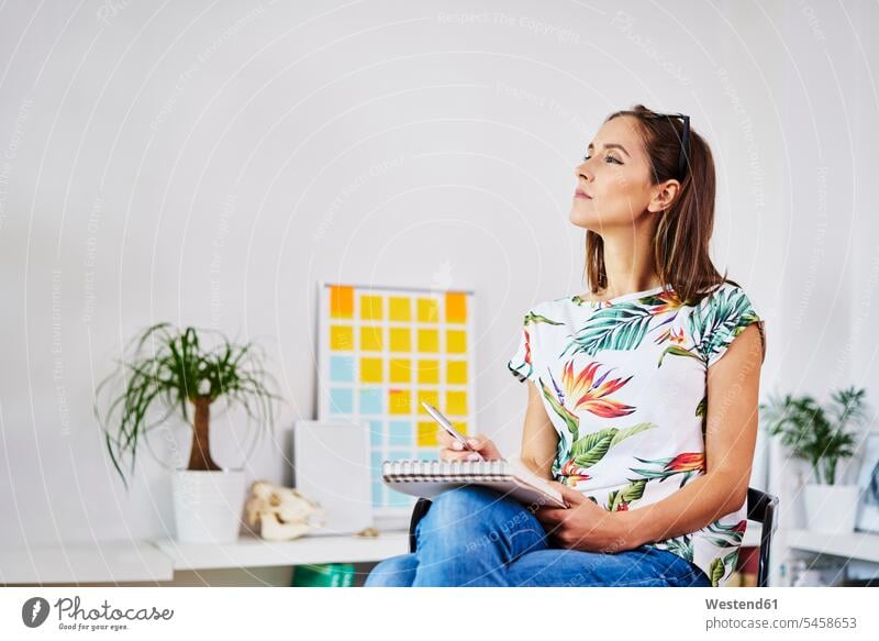 Nachdenkliche junge Frau sitzt auf einem Stuhl und macht sich Notizen notieren Stuehle Stühle Zuhause zu Hause daheim weiblich Frauen denken nachdenken