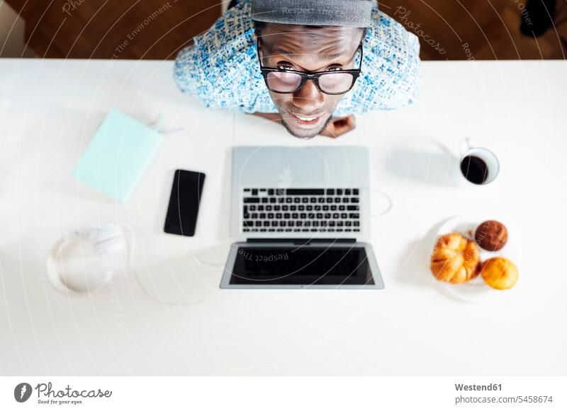 Porträt eines jungen Mannes am Schreibtisch sitzend mit Laptop im Heimbüro Farbaufnahme Farbe Farbfoto Farbphoto Innenaufnahme Innenaufnahmen innen drinnen