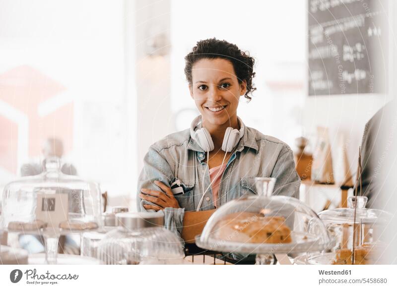 Frau mit Kopfhörern steht mit verschränkten Armen im Café Kuchen arbeiten Arbeit weiblich Frauen Kopfhoerer Cafe Kaffeehaus Bistro Cafes Cafés Kaffeehäuser