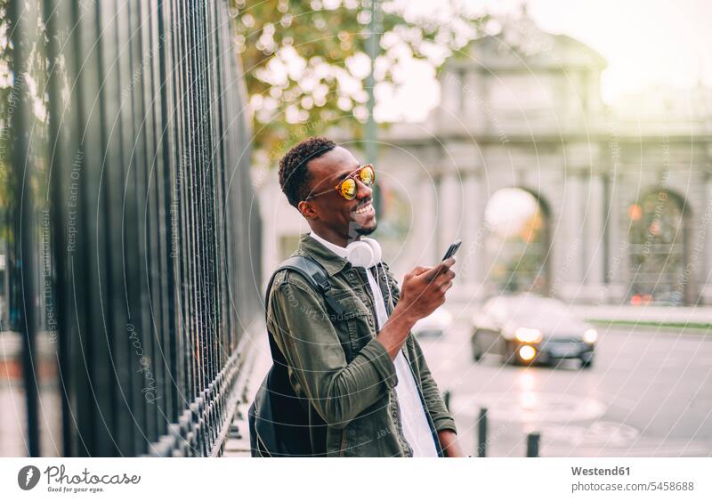 Lächelnder Mann mit Sonnenbrille, der ein Smartphone benutzt, während er in der Stadt steht Farbaufnahme Farbe Farbfoto Farbphoto Spanien Freizeitbeschäftigung