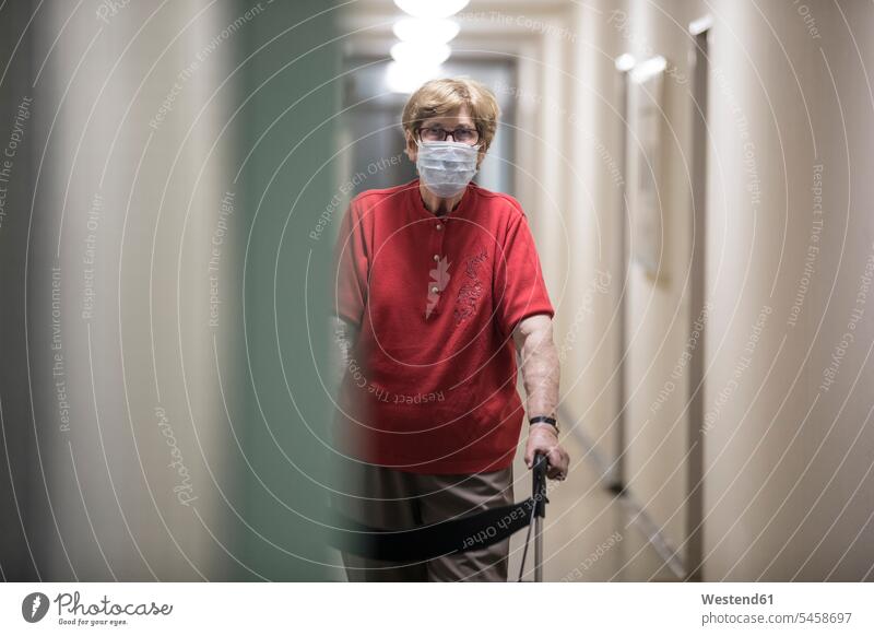 Ältere Frau mit Maske und Gehhilfe auf Rädern im Flur des Altenheims Brillen gehend geht stehend steht daheim zu Hause hygienisch riskant Wagnis geschützt