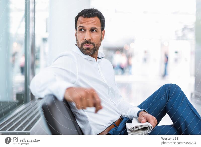 Geschäftsmann mit einer Zeitung in der Wartehalle Zeitungen Mann Männer männlich lesen Lektüre warten umherblicken umschauen umsehen Businessmann Businessmänner