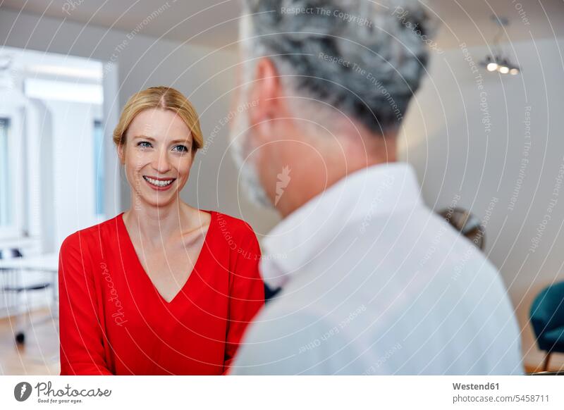 Lächelnde junge Frau schaut auf reifen Kollegen im Büro Arbeitskollegen Kollegin Kolleginnen Office Büros ansehen lächeln Arbeitsplatz Arbeitsstätte