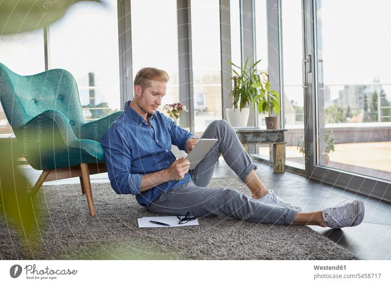 Junger Mann sitzt auf Teppich zu Hause mit Tablet Tablet Computer Tablet-PC Tablet PC iPad Tablet-Computer Männer männlich Teppiche sitzen sitzend Zuhause