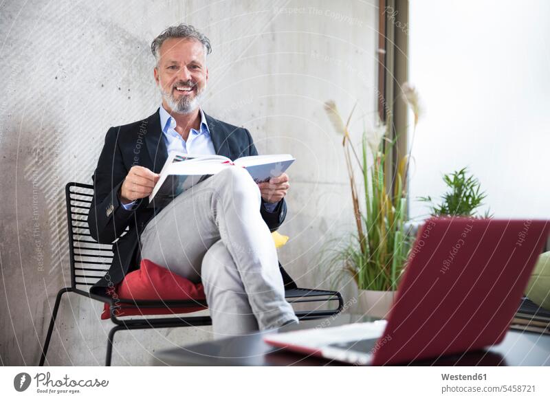 Porträt eines glücklichen Geschäftsmannes, der an einer Betonwand sitzt und ein Buch liest sitzen sitzend Portrait Porträts Portraits Businessmann