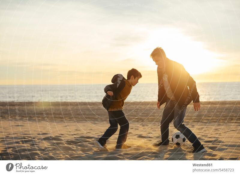 Vater und Sohn spielen bei Sonnenuntergang am Strand Fussball Papas Väter Vati Vatis Papis Beach Straende Strände Beaches Söhne Fußball Fußbälle