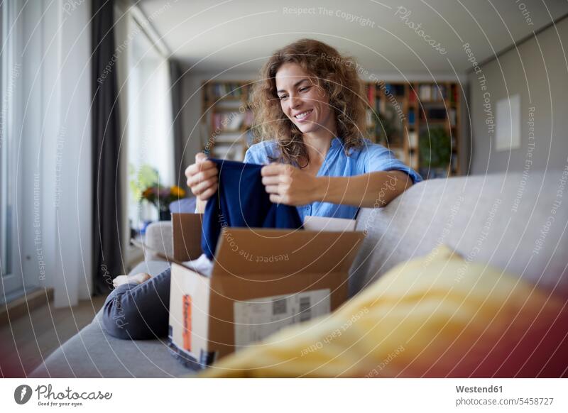 Lächelnde Frau, die zu Hause auf dem Sofa sitzend Stoff aus der Verpackung nimmt Farbaufnahme Farbe Farbfoto Farbphoto Innenaufnahme Innenaufnahmen innen