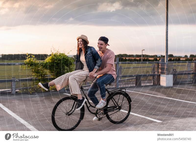 Glückliches junges Paar zusammen auf einem Fahrrad auf dem Parkdeck Leute Menschen People Person Personen Europäisch Kaukasier kaukasisch 2 2 Menschen