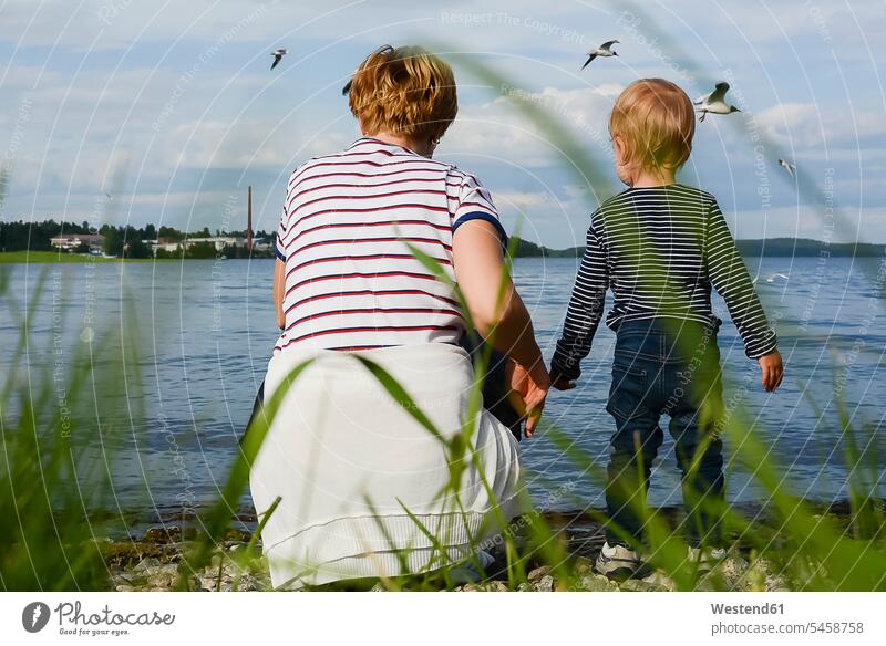 Finnland, Kuopio, Rückenansicht von Mutter und kleiner Tochter, die Möwen am Seeufer beobachten Moewe Laridae Moewen betrachten betrachtend Töchter Mami Mutti