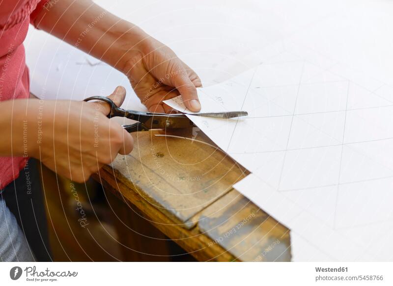 Nahaufnahme einer Frau, die in einer Glaserwerkstatt Papier vom Entwurf abschneidet schneiden arbeiten Arbeit Papiere Skizze Entwürfe Entwuerfe Skizzen