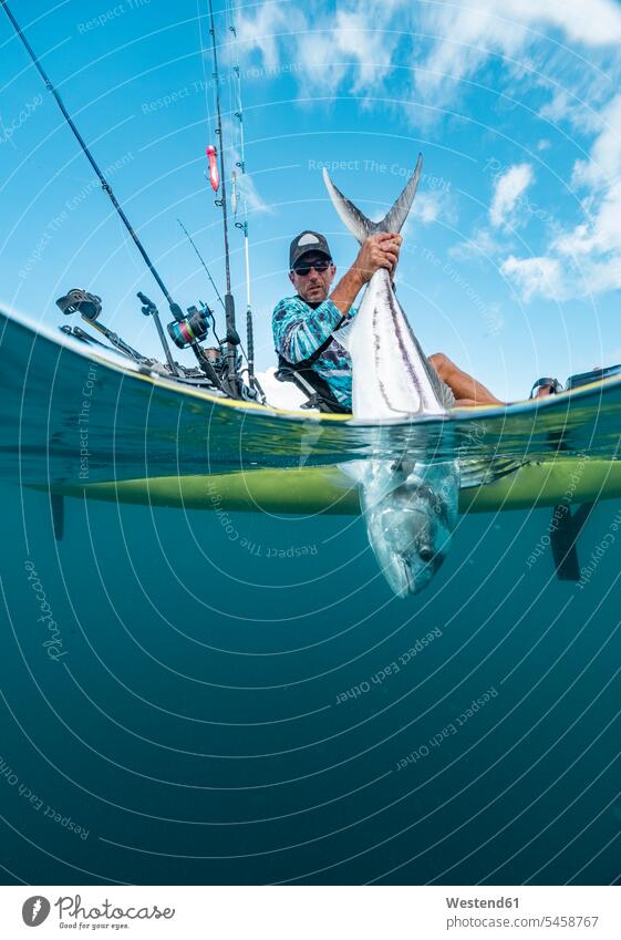 Gespaltener Schuss eines Mannes in einem Kajak beim Fischfang Touristen Tiere Tierwelt Fische Pisces Angeln Angelrute Angelruten Wasserfahrzeug Boote